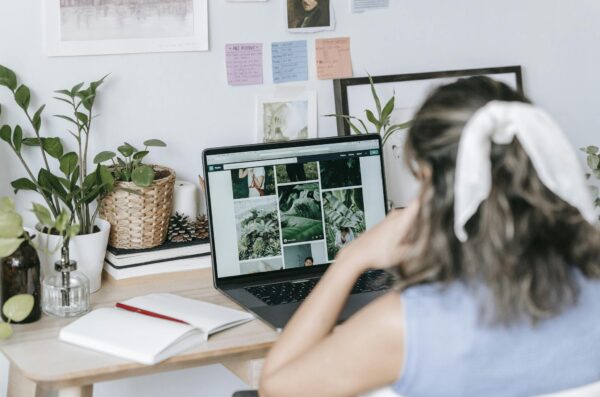 A woman at home working remotely on a laptop surrounded by plants and notes.